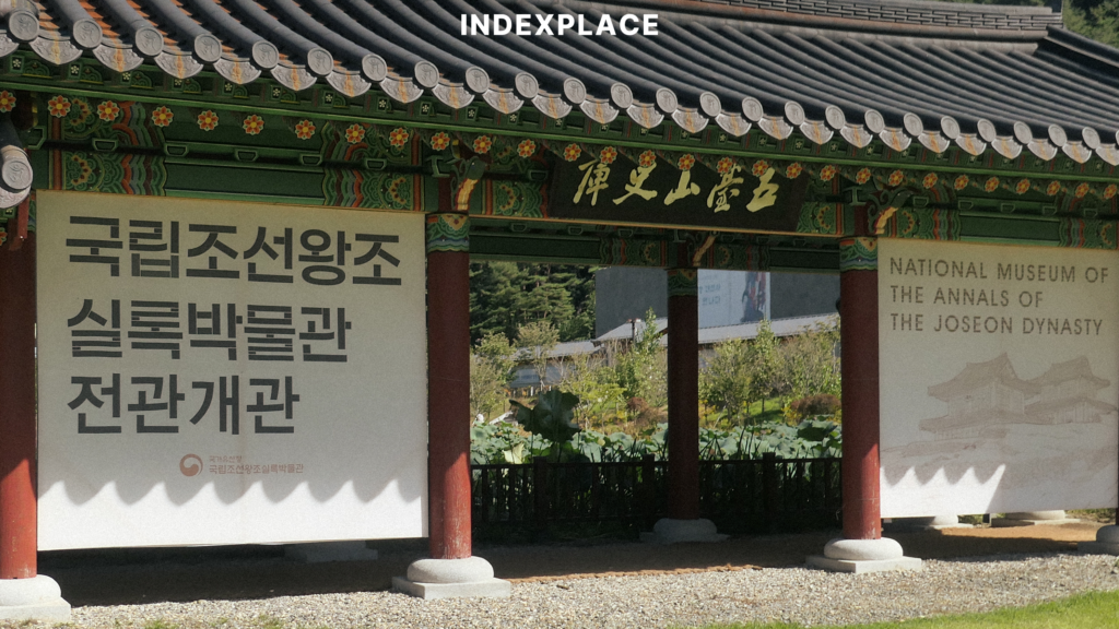 A photograph of a traditional Korean gate serving as an information panel for the National Museum of the Annals of the Joseon Dynasty, as seen in national-museum-of-the-annals-of-the-joseon-dynasty.jpg. Large banners feature text verbatim: on the left, '국립조선왕조실록박물관 전관개관', and on the right, 'NATIONAL MUSEUM OF THE ANNALS OF THE JOSEON DYNASTY'.